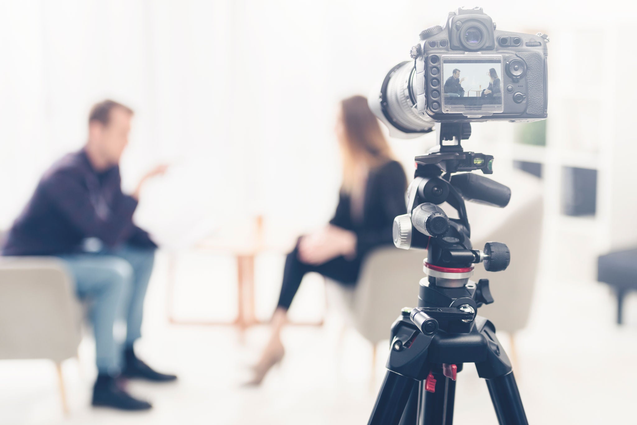 businesswoman in suit giving interview to journalist in office, camera on tripod on foreground